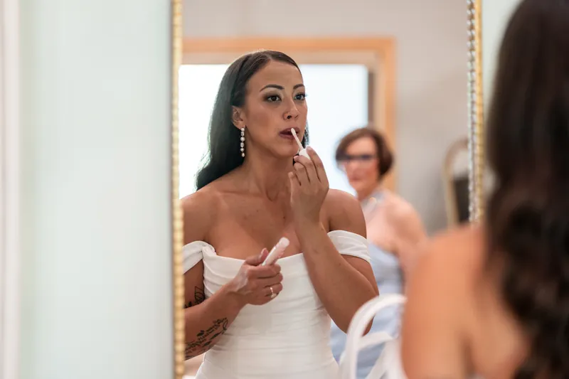Bride applying lipstick in a gold-framed mirror while getting ready