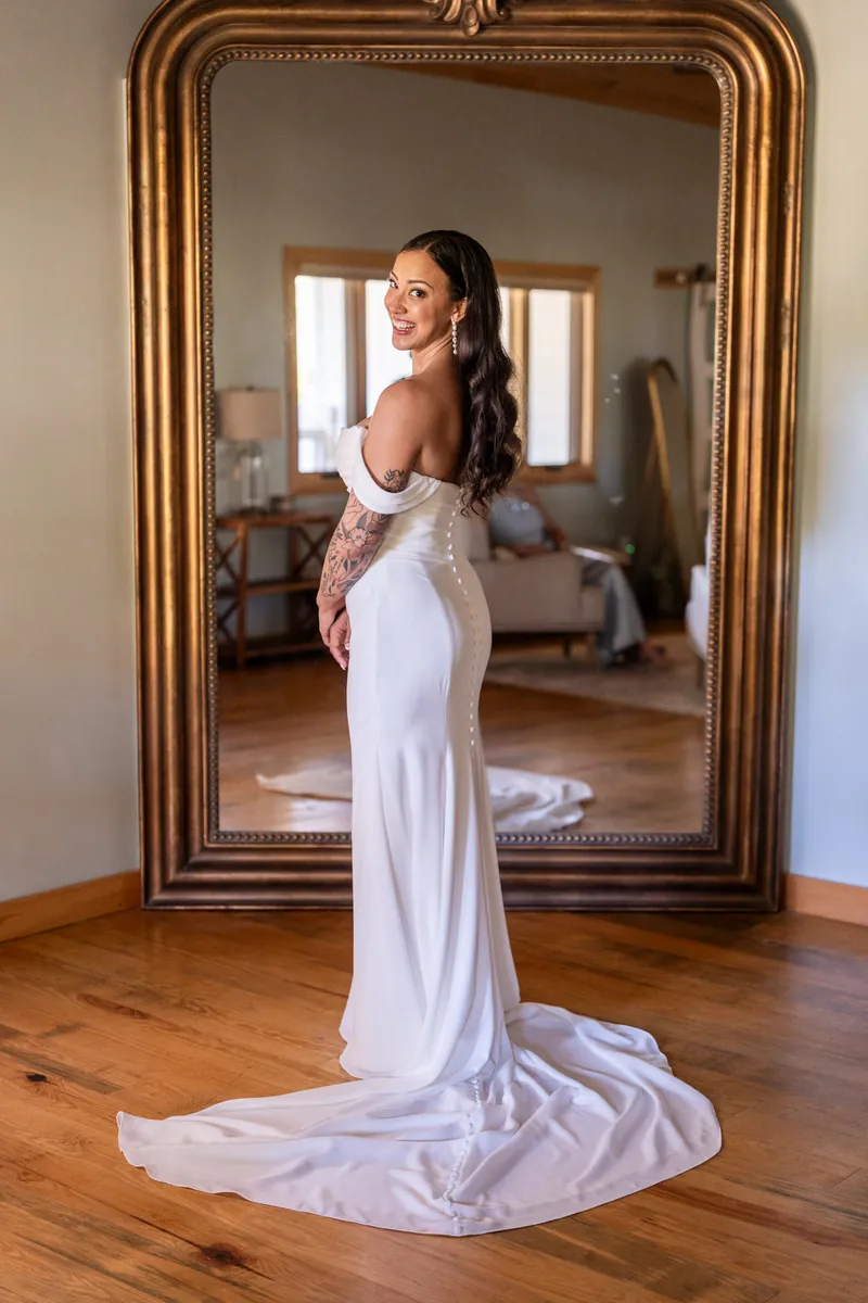 Bride looking over her shoulder showing off dress train and tattoo sleeve in front of mirror
