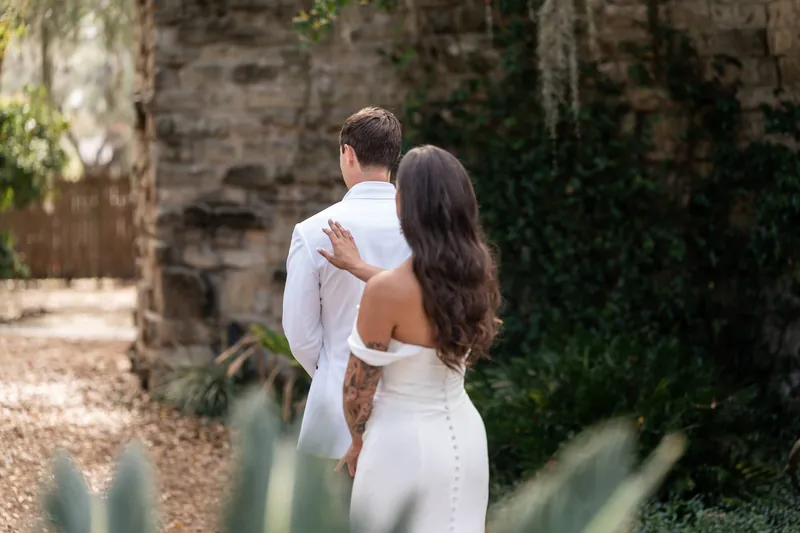 Bride adjusting grooms collar during first look with ivy-covered wall in background