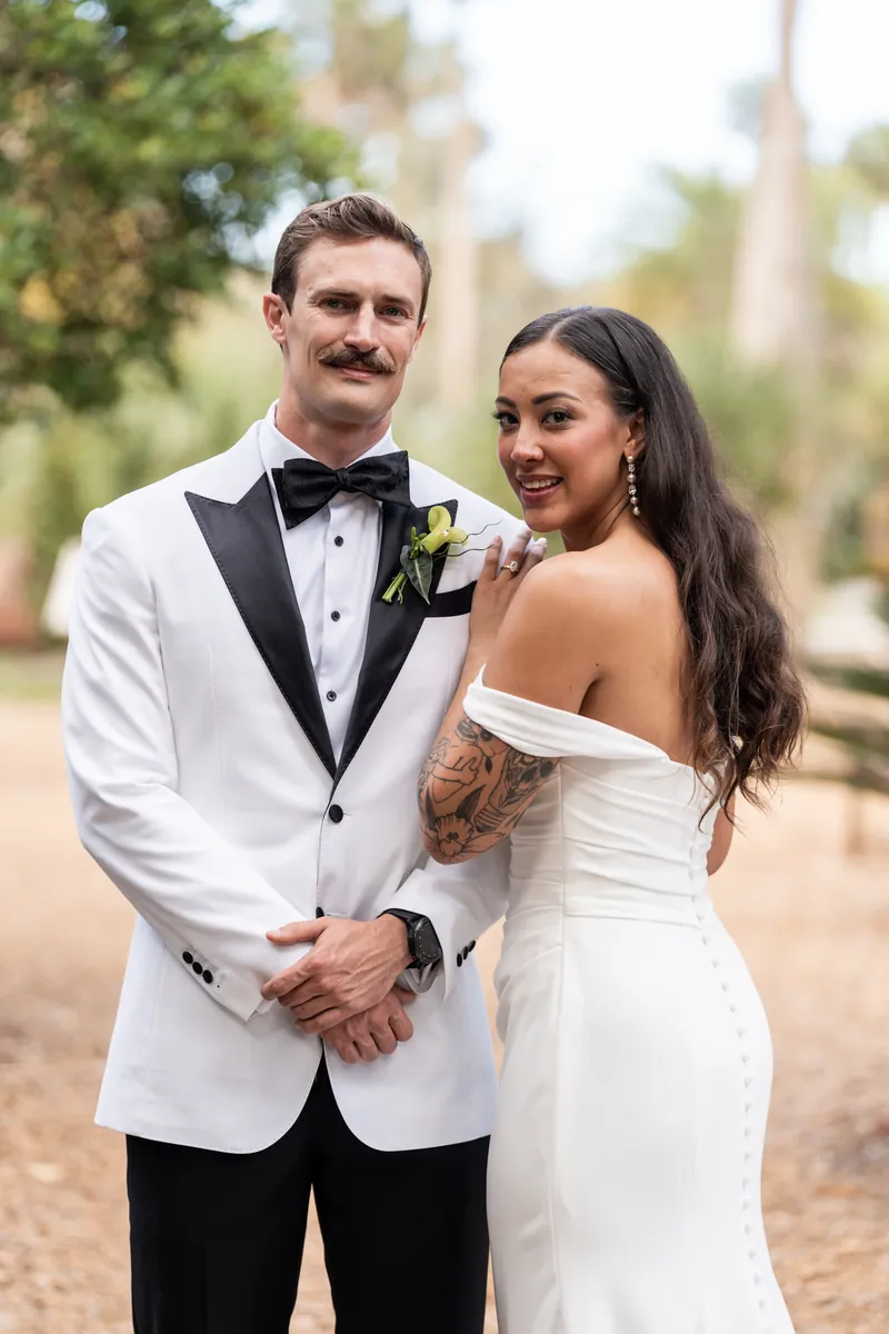 Close up portrait of bride and groom with green boutonniere and off-shoulder dress details