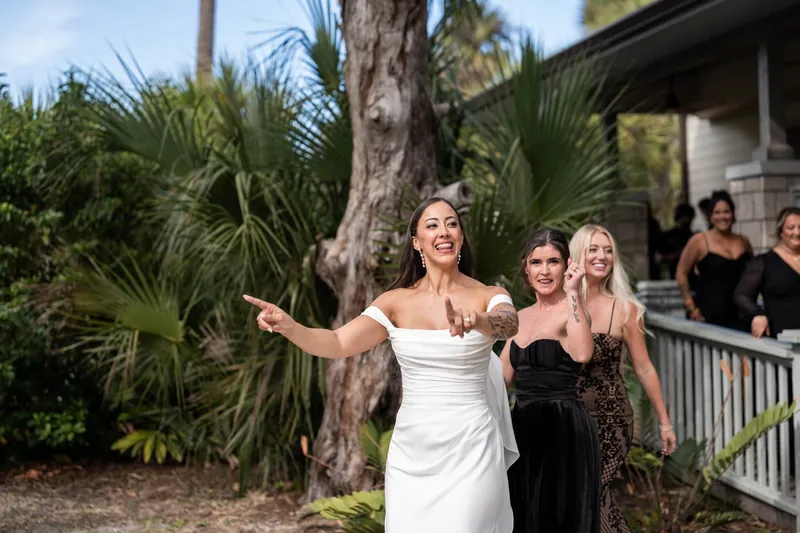 Bride pointing excitedly while walking with bridesmaids near palm trees
