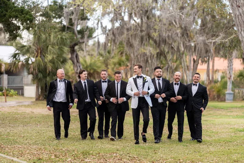 Groom and eight groomsmen walking together in black tuxedos under Spanish moss