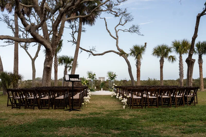 Wide view of outdoor ceremony setup with dark wood chairs and white round stage under oak trees