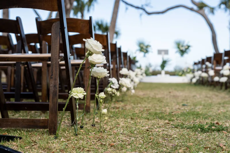 White roses placed along the ground next to dark wooden ceremony chairs