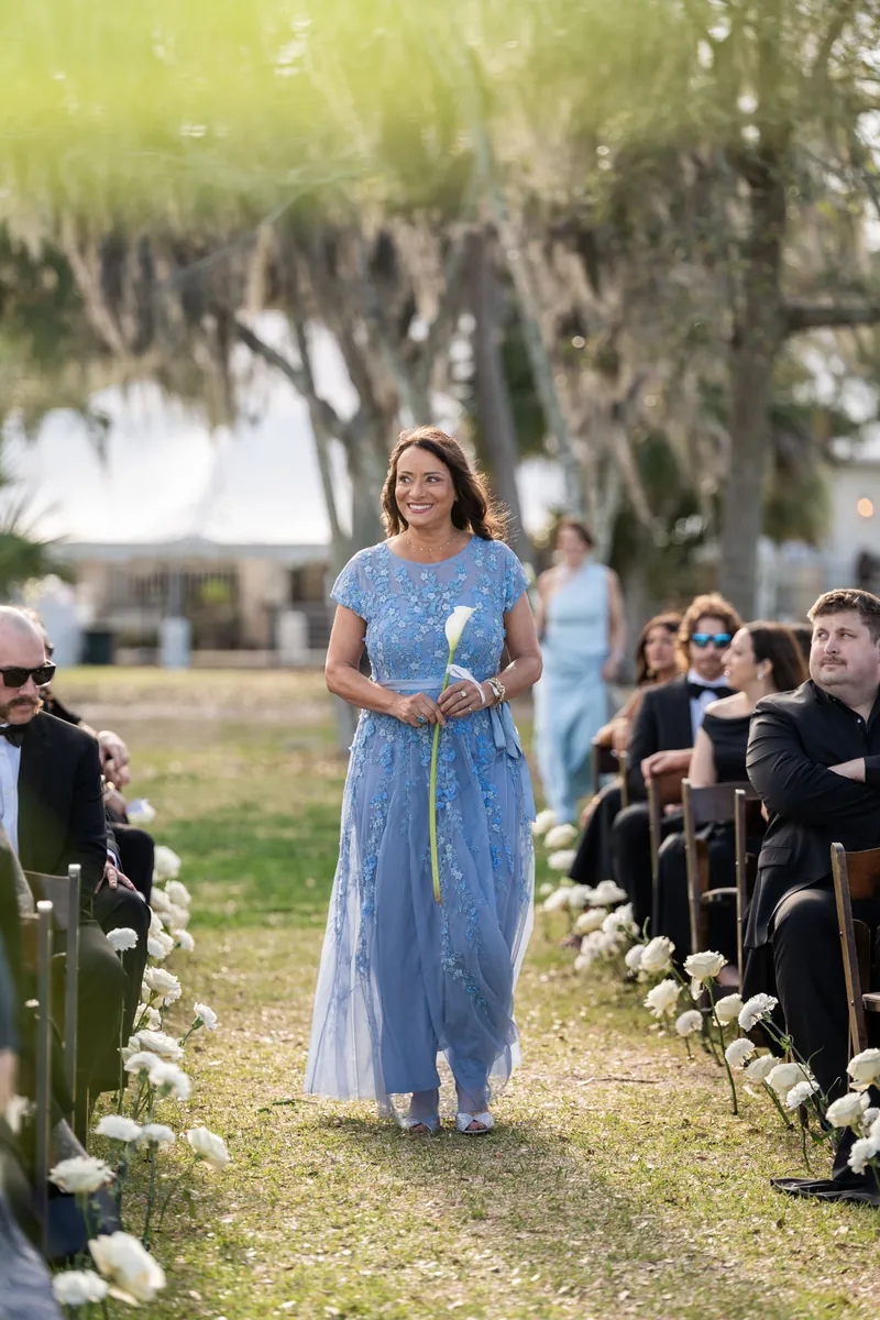 Bridesmaid walking down the aisle in black off-shoulder dress under Spanish moss