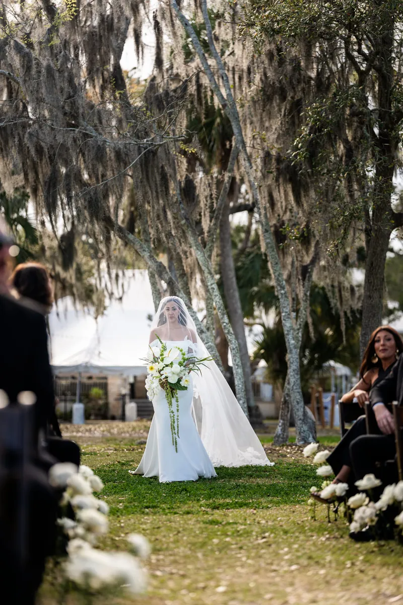 Bride processing down the aisle with veil flowing among seated guests