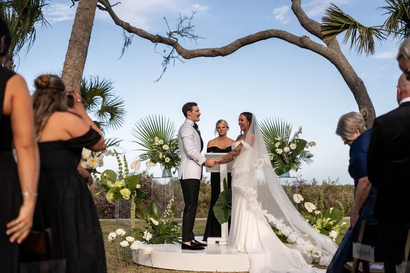 Bride and groom at the altar with officiant and tropical floral arrangements on acrylic stands