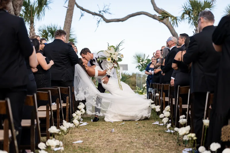 Groom dipping bride for a kiss during recessional as guests cheer with paper airplanes