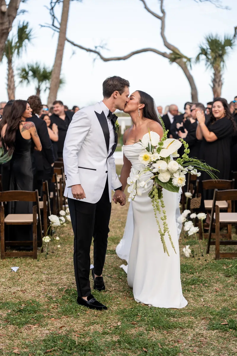 Bride and groom sharing a kiss during the recessional with guests applauding behind them