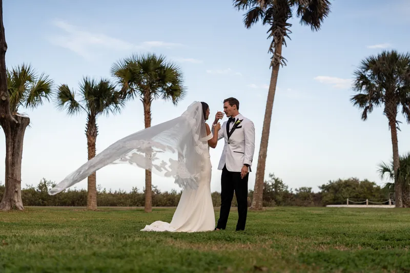Bride and groom with veil blowing in the wind among palm trees on the Fountain of Youth lawn