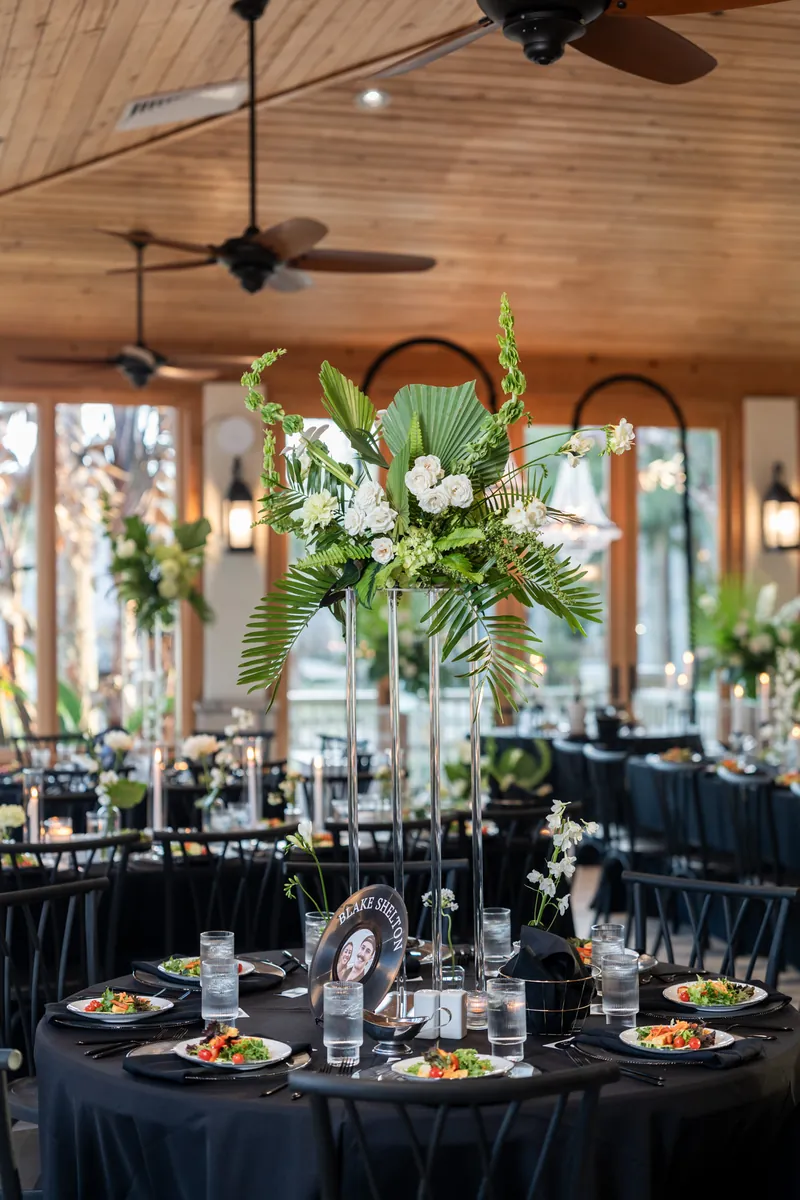Reception table with tall tropical centerpiece on clear stand and vinyl record table number