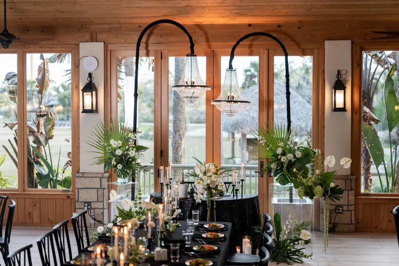 Sweetheart table with chandeliers and tropical floral arrangements in warm reception lighting
