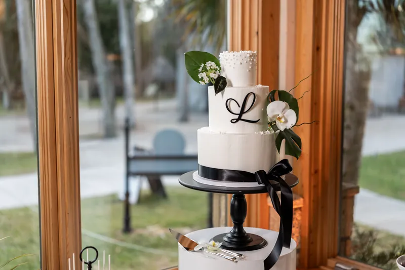 Three-tier white wedding cake with black ribbon and orchid on black stand