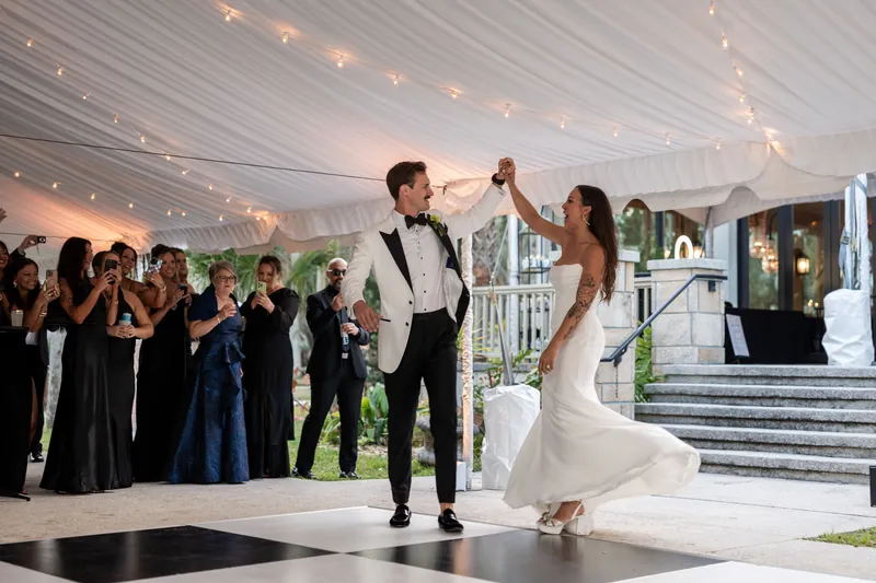 First dance spin on black and white checkered dance floor under tent with string lights