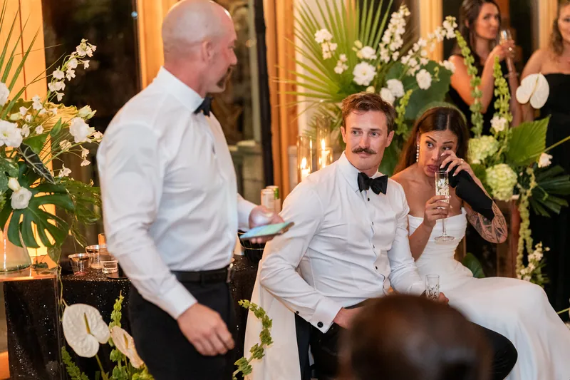 Best man giving toast while Michelle wipes tears and Bryant watches