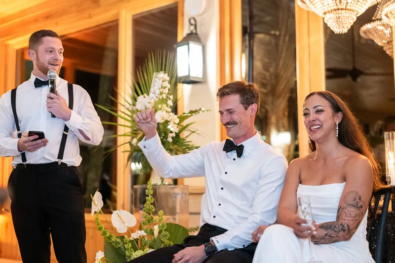 Groomsman giving speech while Bryant raises hand and Michelle laughs