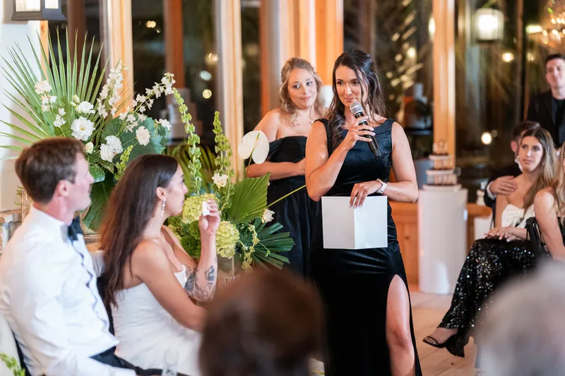 Maid of honor giving toast during reception as couple listens from sweetheart table