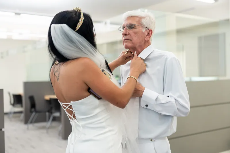 A person in a white strapless dress adjusts the tie of someone in a light blue shirt at St. Johns County Courthouse.