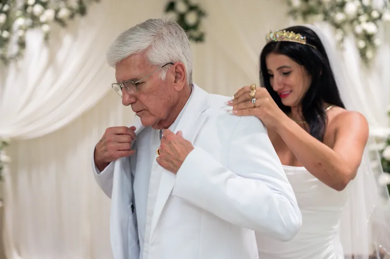 One partner fastens the other's tie while both smile during their courthouse elopement.