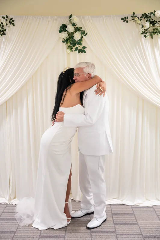 The couple embraces tightly, Isury's arm around Mike's shoulder in their coordinated white ceremony attire.