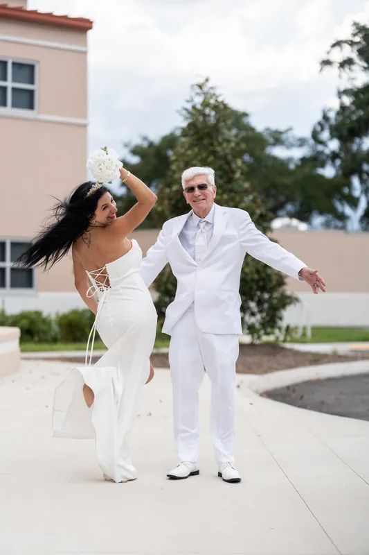 Mike reaches toward Isury mid-laugh as they celebrate on the sun-lit courthouse grounds, her veil flowing behind her.