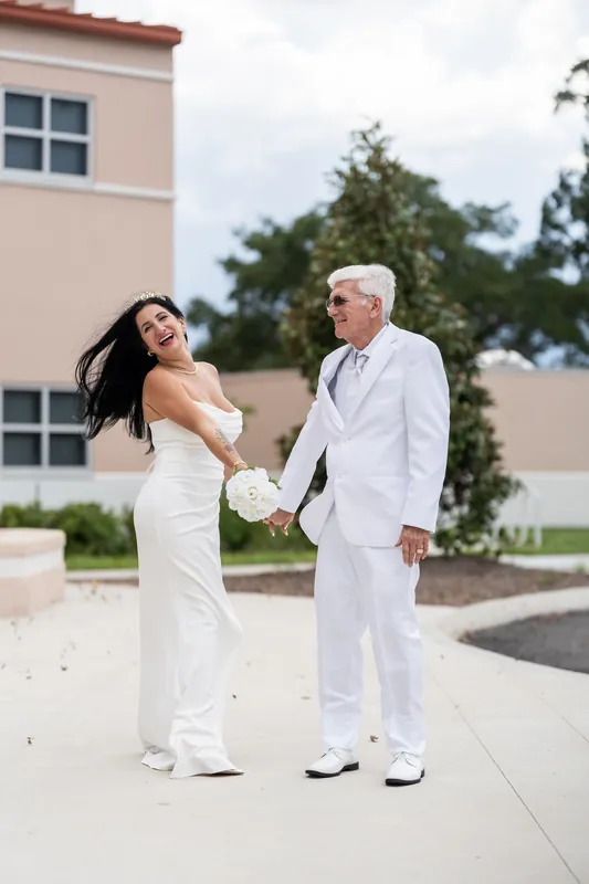 Isury playfully nudges Mike while they pose together on the courthouse walkway, bouquet in hand.