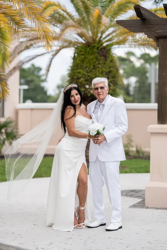 Isury leans against Mike under palm fronds on the courthouse grounds in soft natural light.