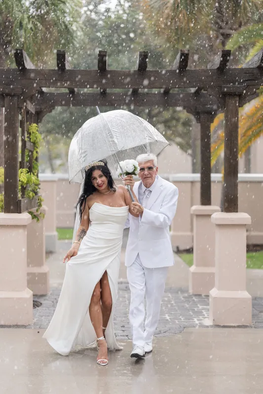Rain falls around Isury and Mike as they stand under an umbrella near the pergola structure at the courthouse grounds.