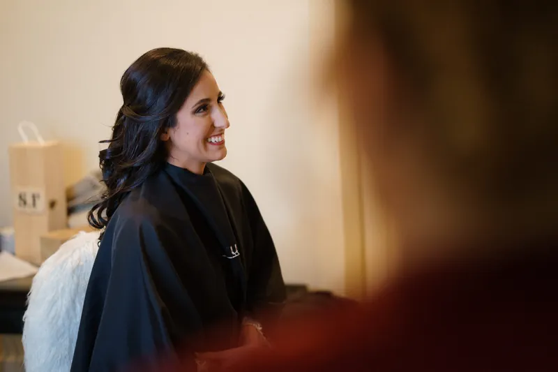 Monica smiles while looking to the side, wearing a black jacket with the museum's soft morning light behind her.