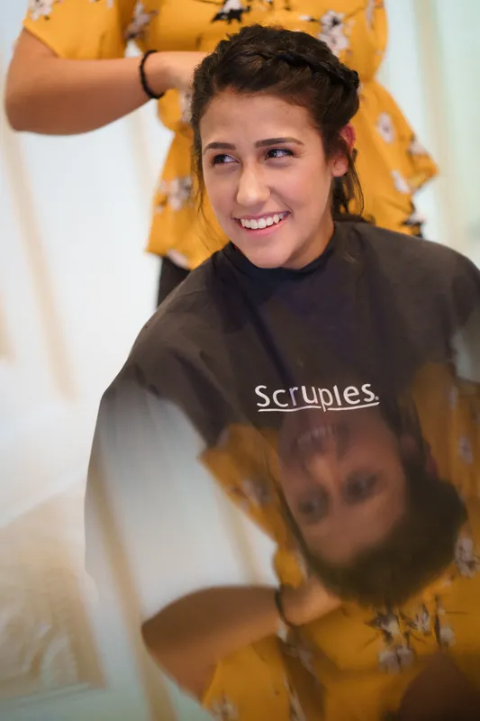 Someone in a yellow floral shirt helps Monica with her hair as she grins at The Oldest House Museum.