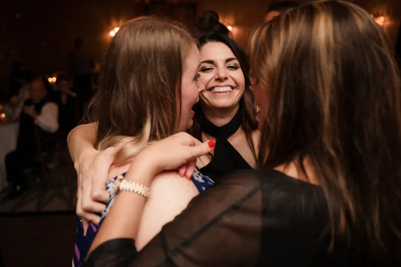Three guests embrace in a group hug, smiling and celebrating on the dance floor.