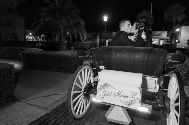 Monica and Michael depart in a vintage carriage displaying a "Just Married" sign under the resort's nighttime lights.