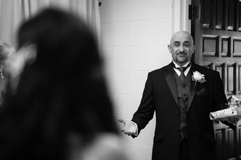 Michael grins as he holds Monica's hand during their first look, standing in front of a white colonial-style door.