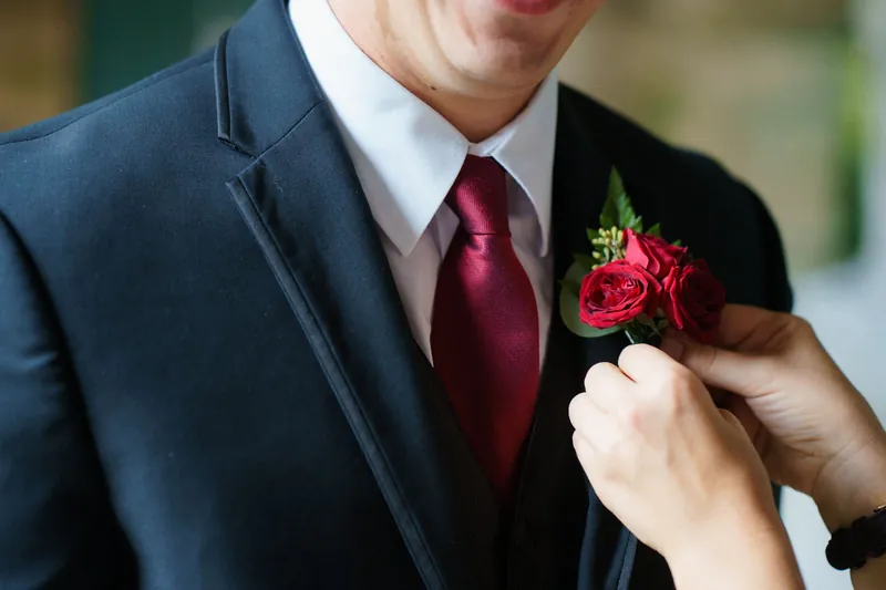 Someone pins a red and white boutonniere on Michael's navy jacket lapel.