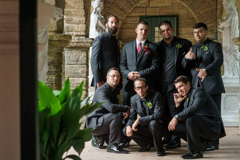 Michael stands with seven groomsmen in dark suits along the colonnade at The Oldest House Museum, St. Augustine.