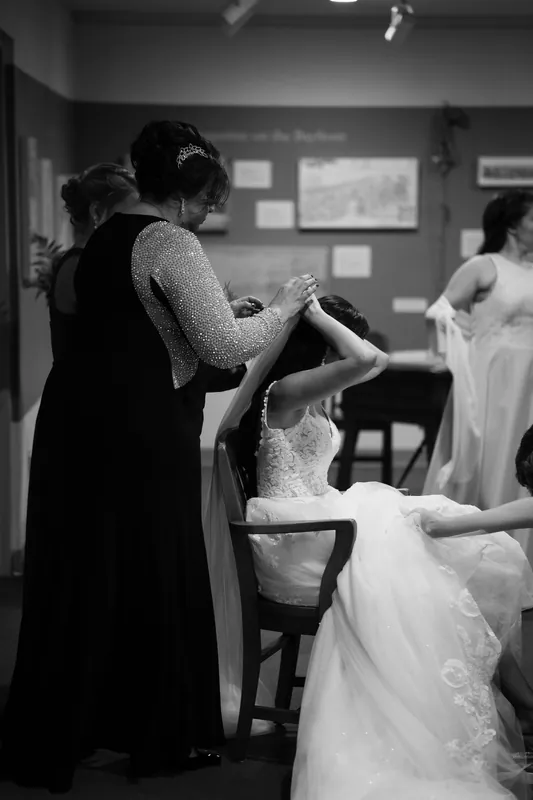 Monica adjusts her white lace gown while a family member helps fasten her dress before the ceremony.