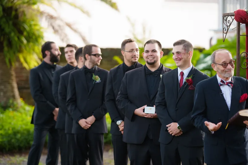Michael walks alongside six groomsmen in black suits across the manicured lawn at The Oldest House Museum, St. Augustine.