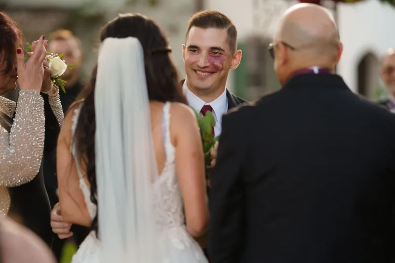 Michael smiles at Monica during their ceremony at The Oldest House Museum, surrounded by guests in formal attire.