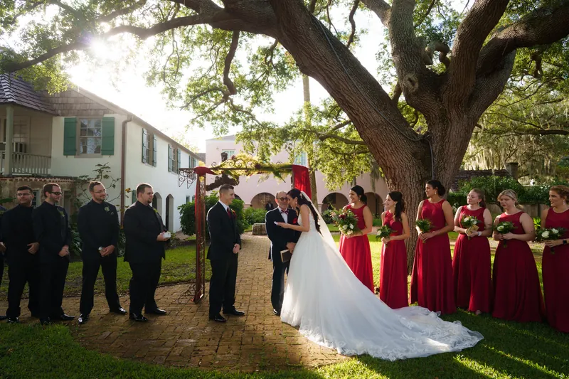 Monica and Michael exchange vows beneath a sprawling oak tree as attendants in burgundy and navy stand witness.