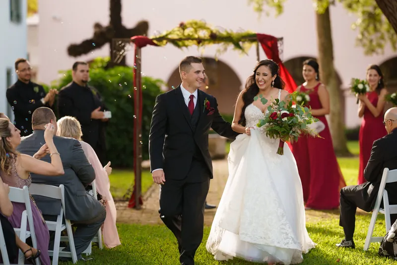 Monica and Michael walk back down the aisle together, hand in hand, as guests seated on either side applaud and celebrate.