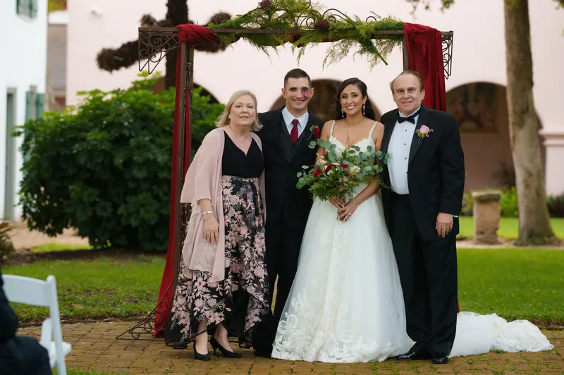 Monica poses with family members beneath the decorated archway, holding her bouquet.