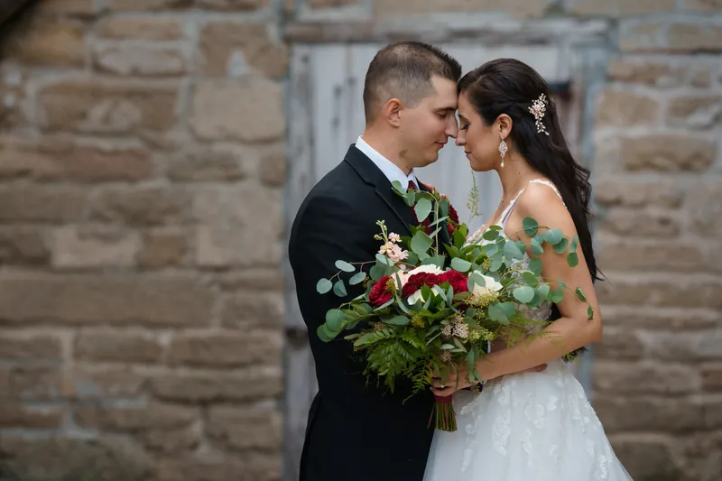 Michael leans in to kiss Monica's cheek as they hold their red and white bouquet together at the museum's entrance.