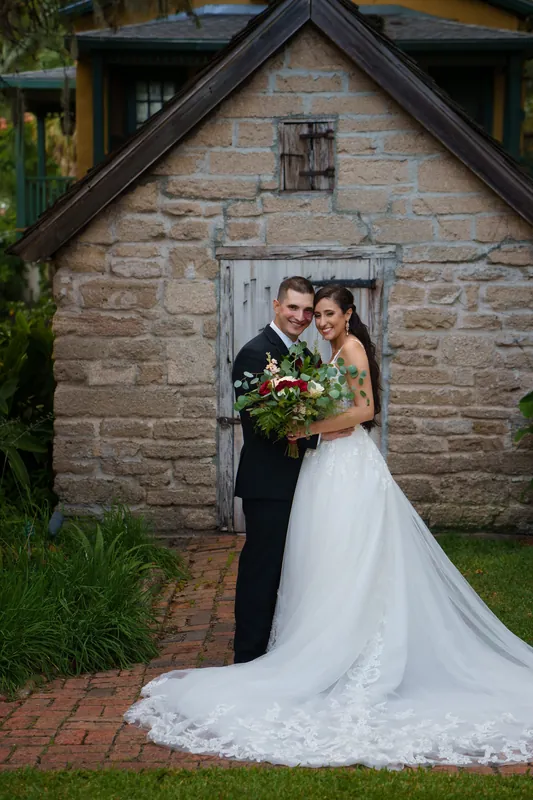 Monica and Michael embrace near the whitewashed wooden door, her long train trailing across the brick pathway behind them.