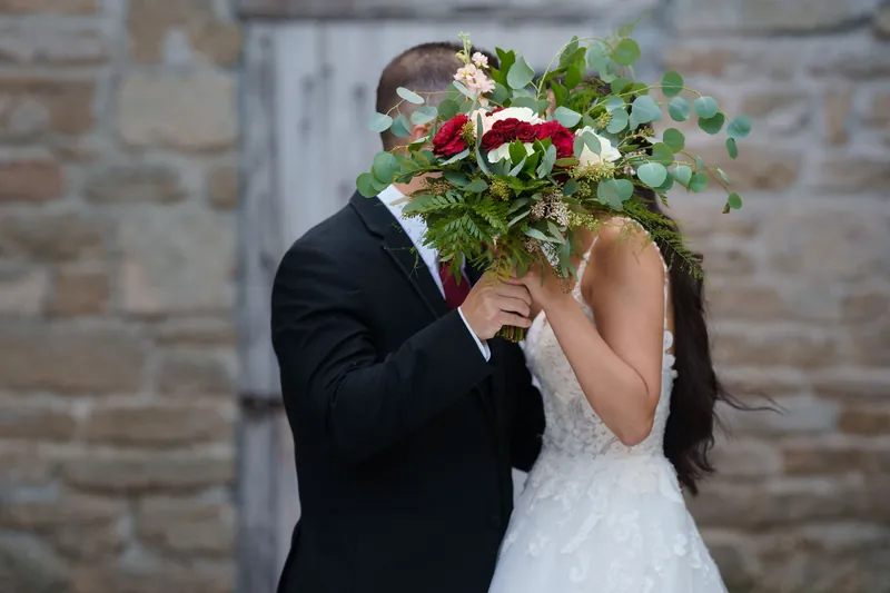 Michael and Monica kiss behind their overflowing bouquet of roses and eucalyptus, their faces hidden by the arrangement.