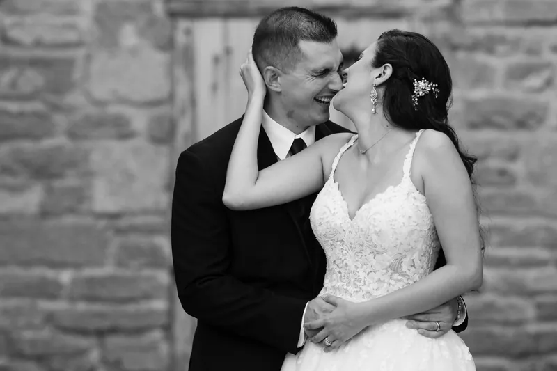 Monica and Michael lean toward each other for a kiss in black and white against the historic stone wall.