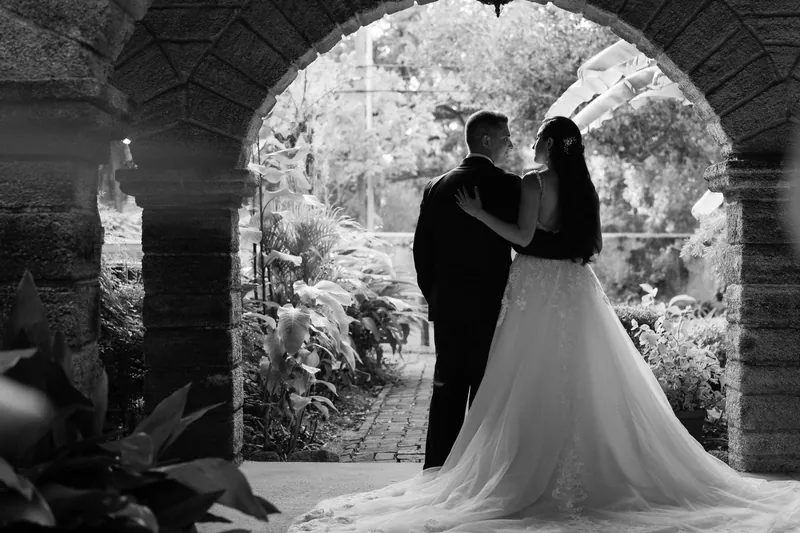Michael and Monica dance under a brick archway with Monica's train flowing behind them in black and white.