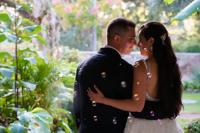 Surrounded by flowering plants and vines, Michael and Monica embrace and laugh together in the museum's garden courtyard.