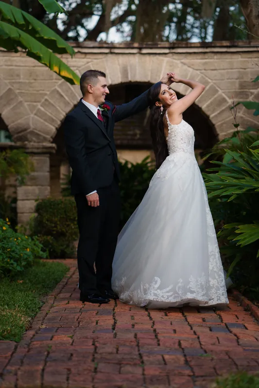 Michael adjusts Monica's hair as she laughs, both framed by the brick archway with lush greenery flanking either side.