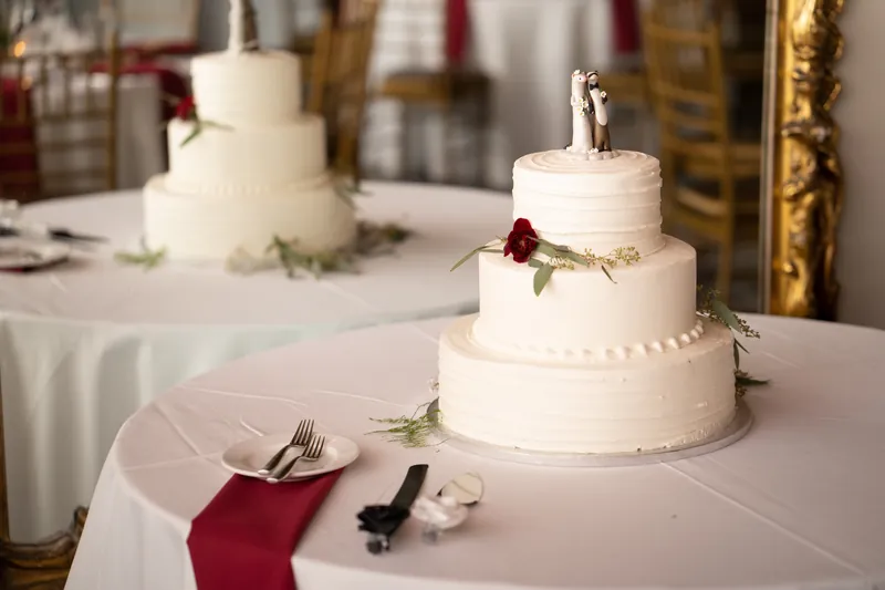Three-tiered wedding cakes with white fondant and burgundy floral accents sit on tables at Casa Monica Resort & Spa.