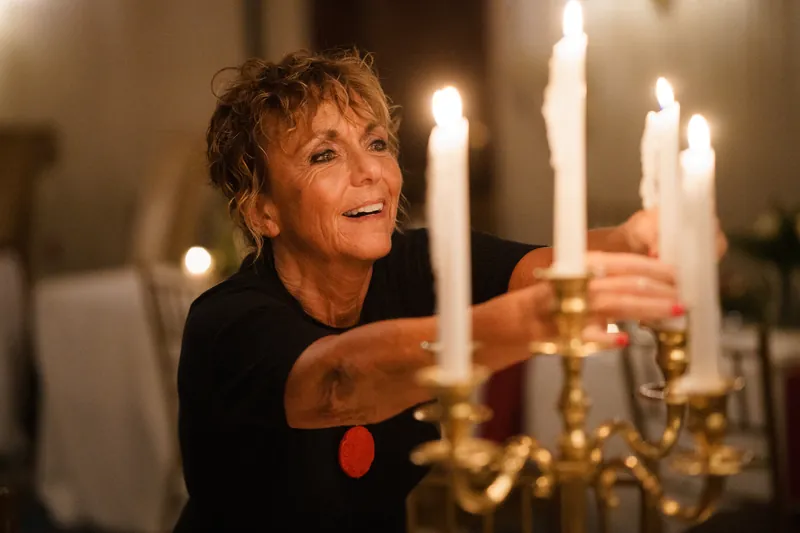 A woman in a black top lights candles in a gold candelabra at the reception.